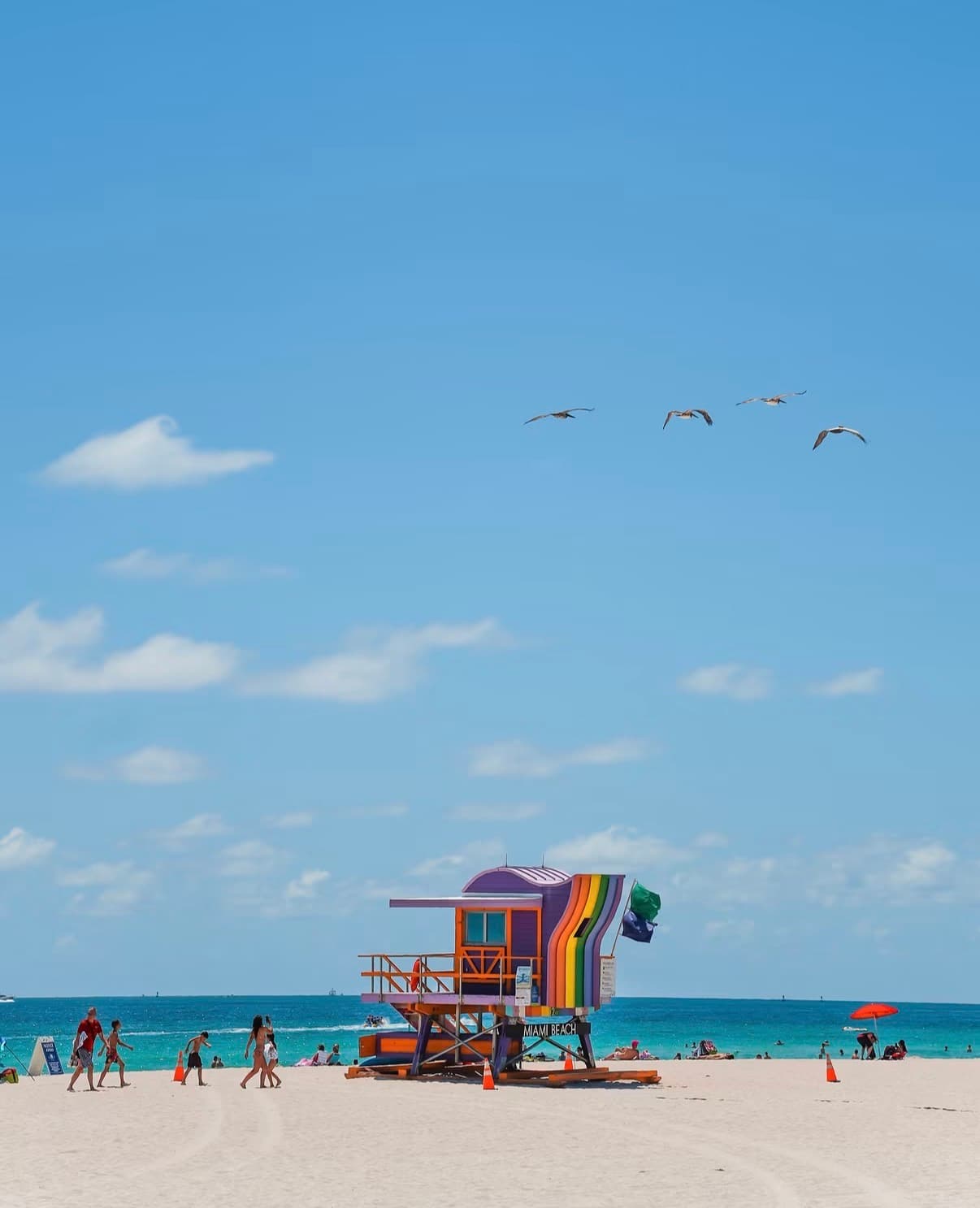 A rainbow lifeguard tower on a busy beach under a blue sky