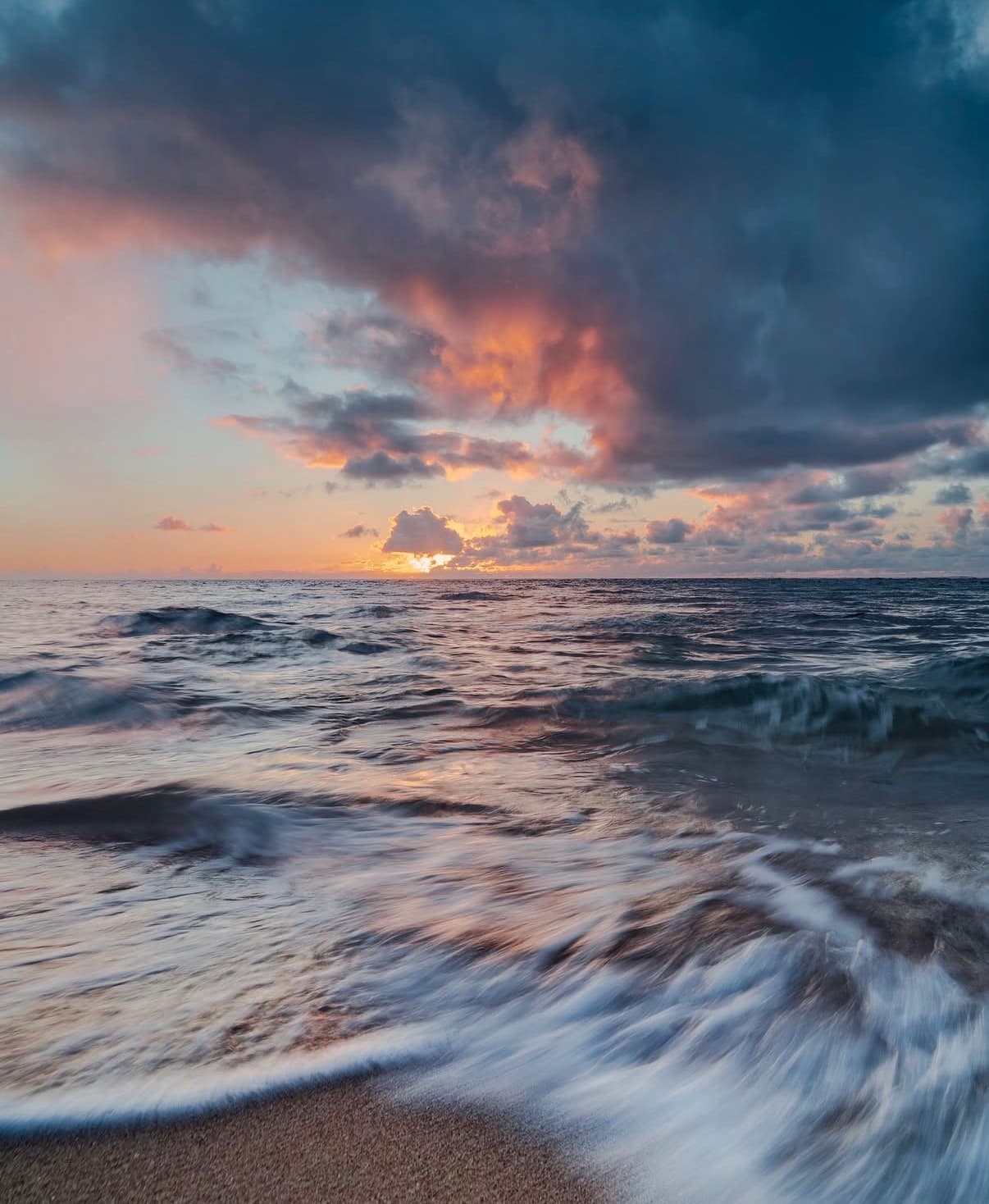 Waves running up a Kauaʻi beach under a pink and grey sunset