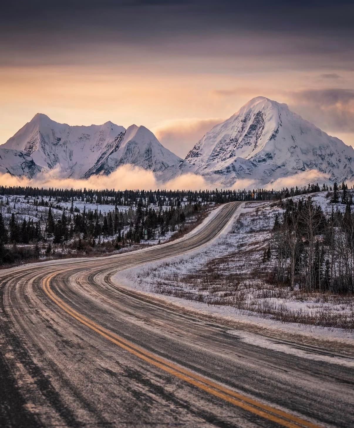 A winding highway through spruce and snow towards Alaska's peaks at dawn