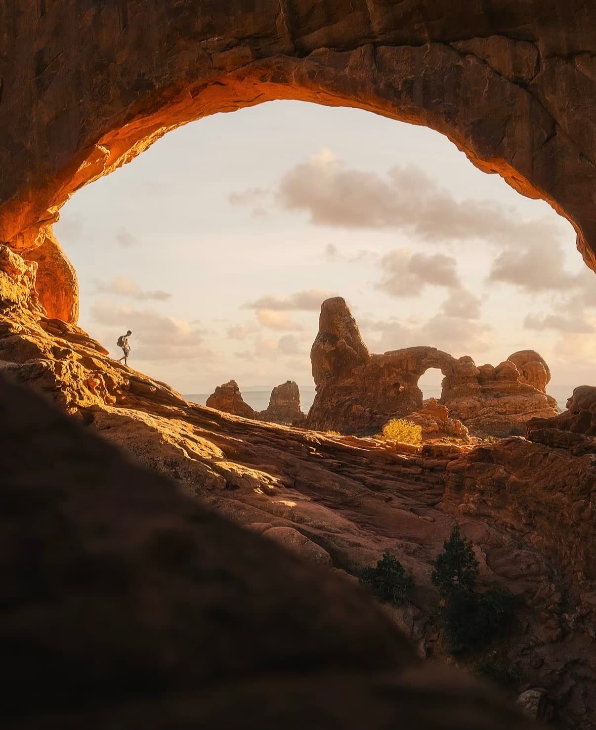 A hiker framed by a sandstone window with Turret Arch beyond