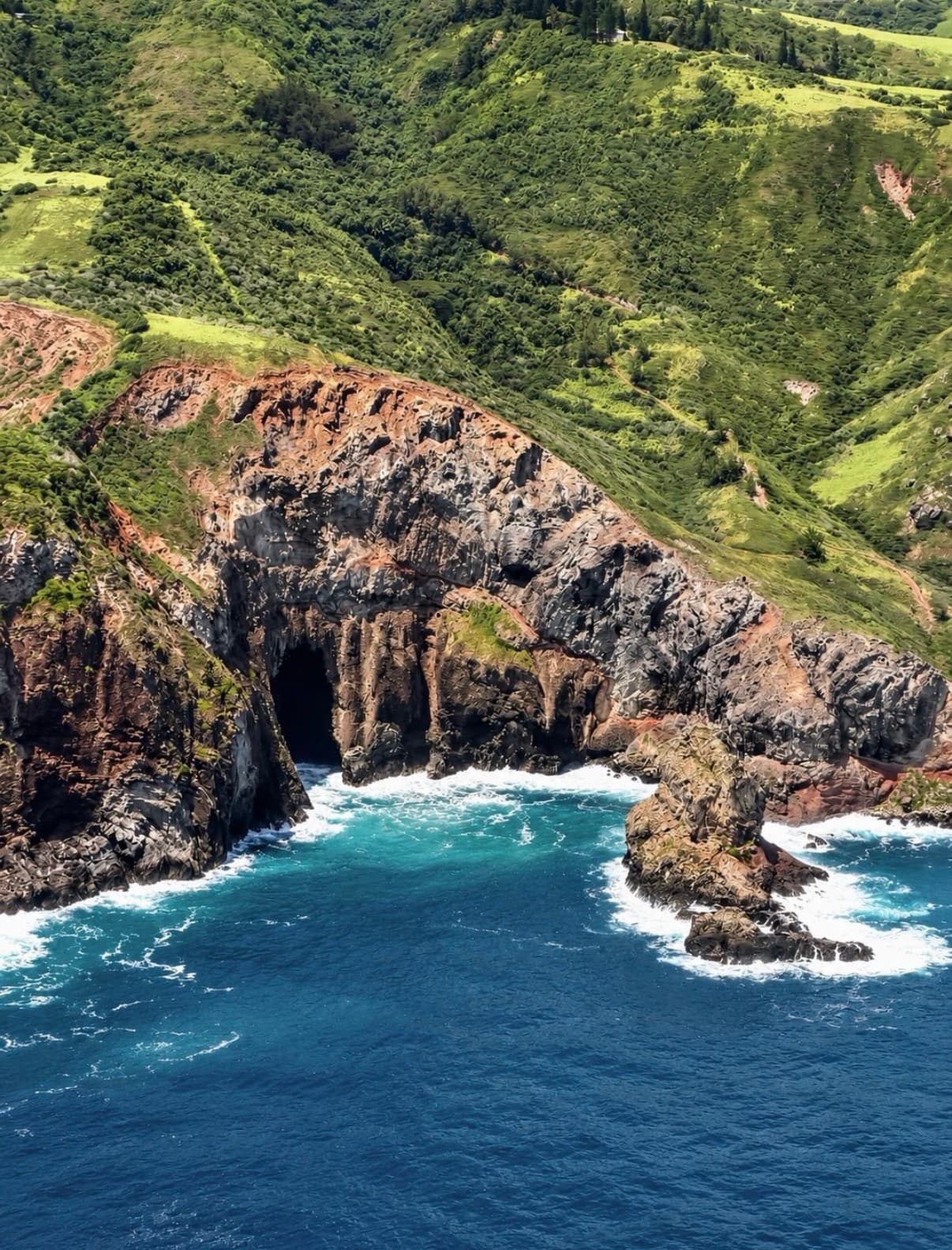 Surf washing into a sea cave below green coastal slopes