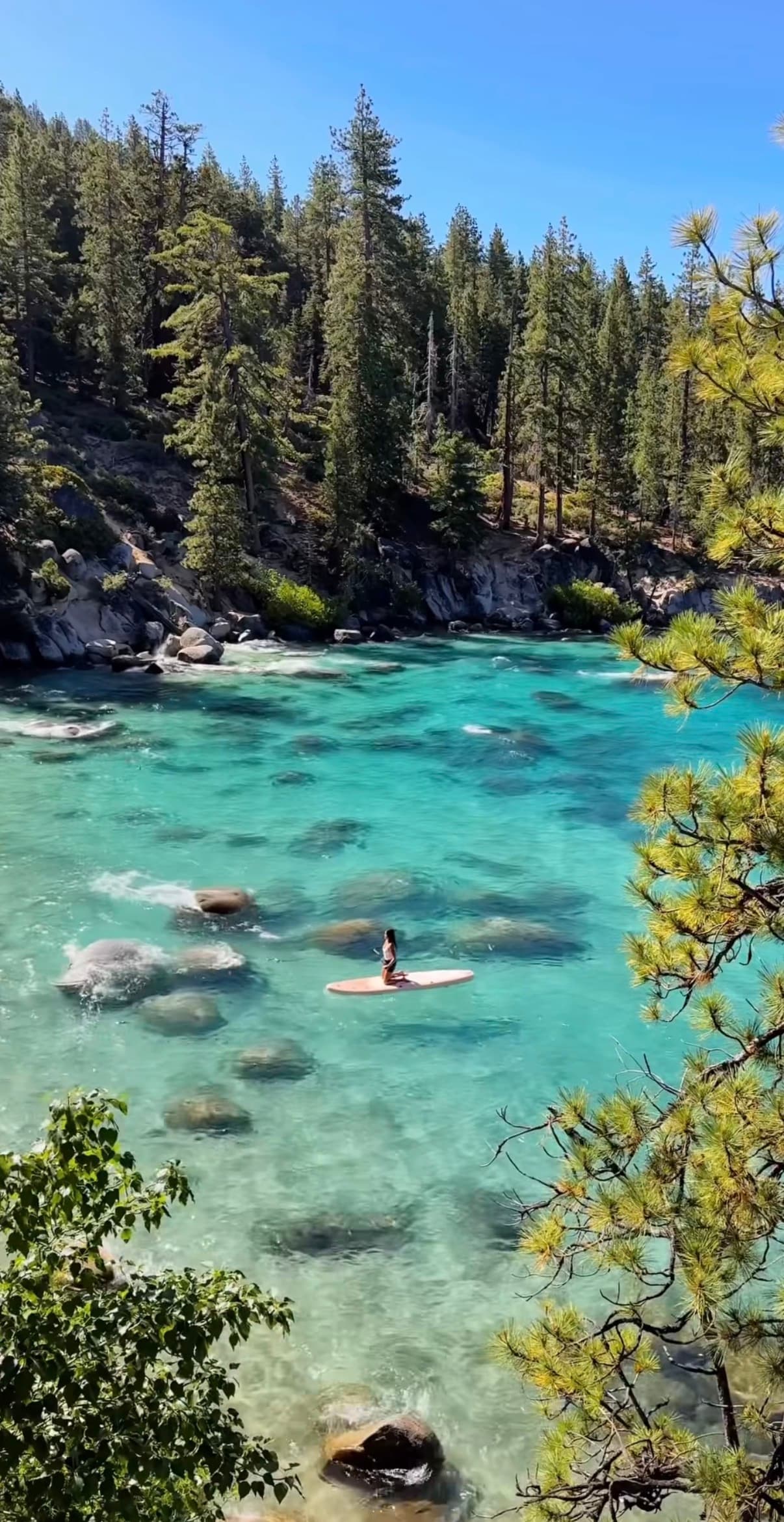A paddleboarder on turquoise water along the Lake Tahoe shore