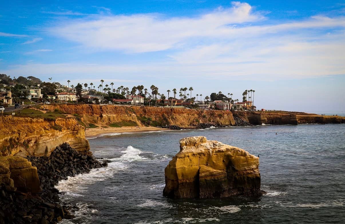A sandstone sea stack below palm-lined coastal cliffs