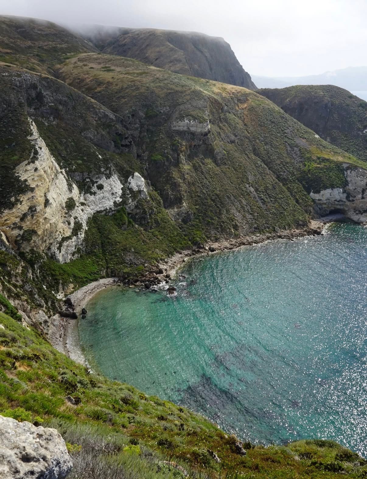 A green coastal canyon opening onto a clear turquoise cove