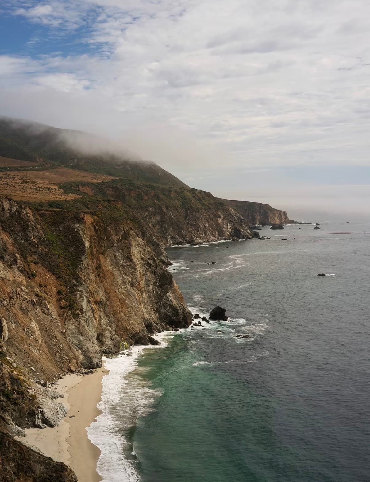 Fog over steep coastal cliffs and a curving beach