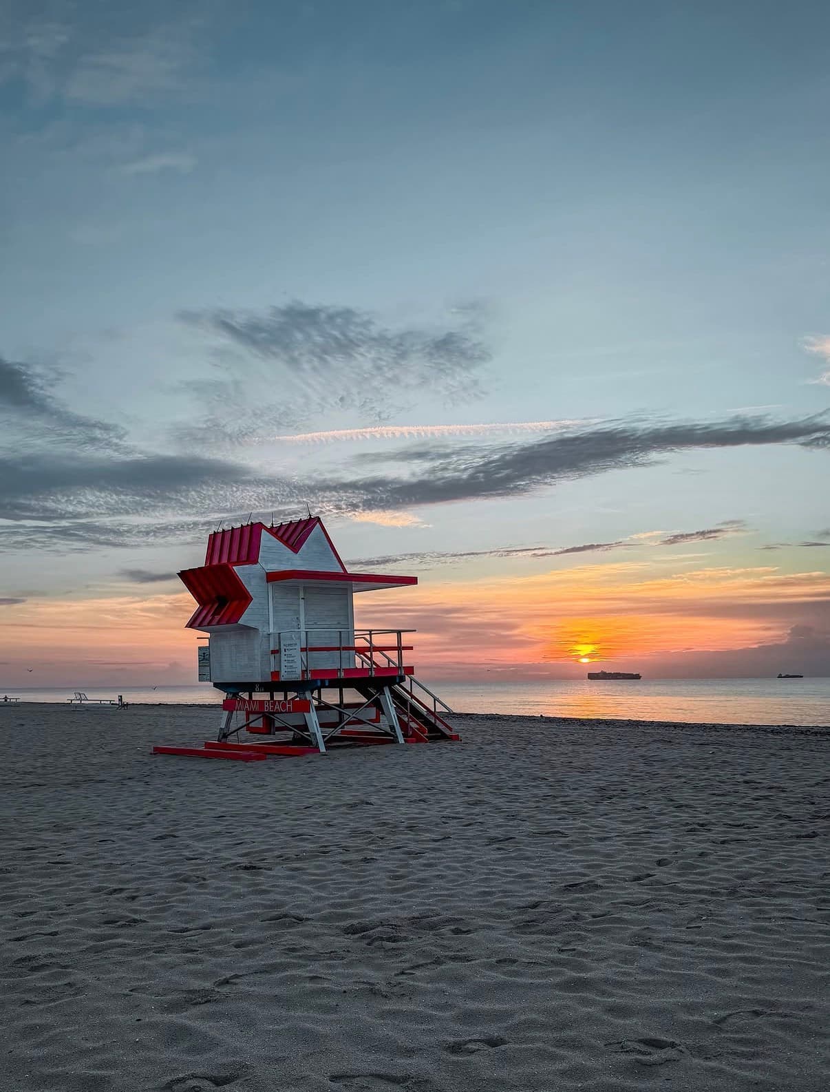 A red-and-white lifeguard tower on the beach at sunset