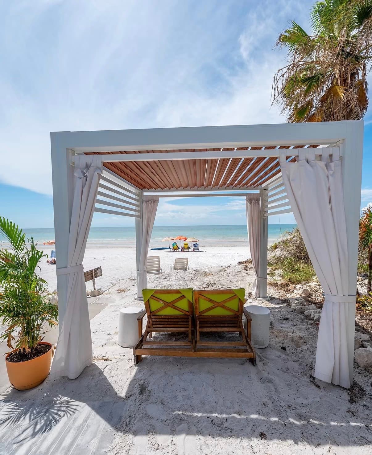 A white beach cabana with two loungers on soft sand by clear water