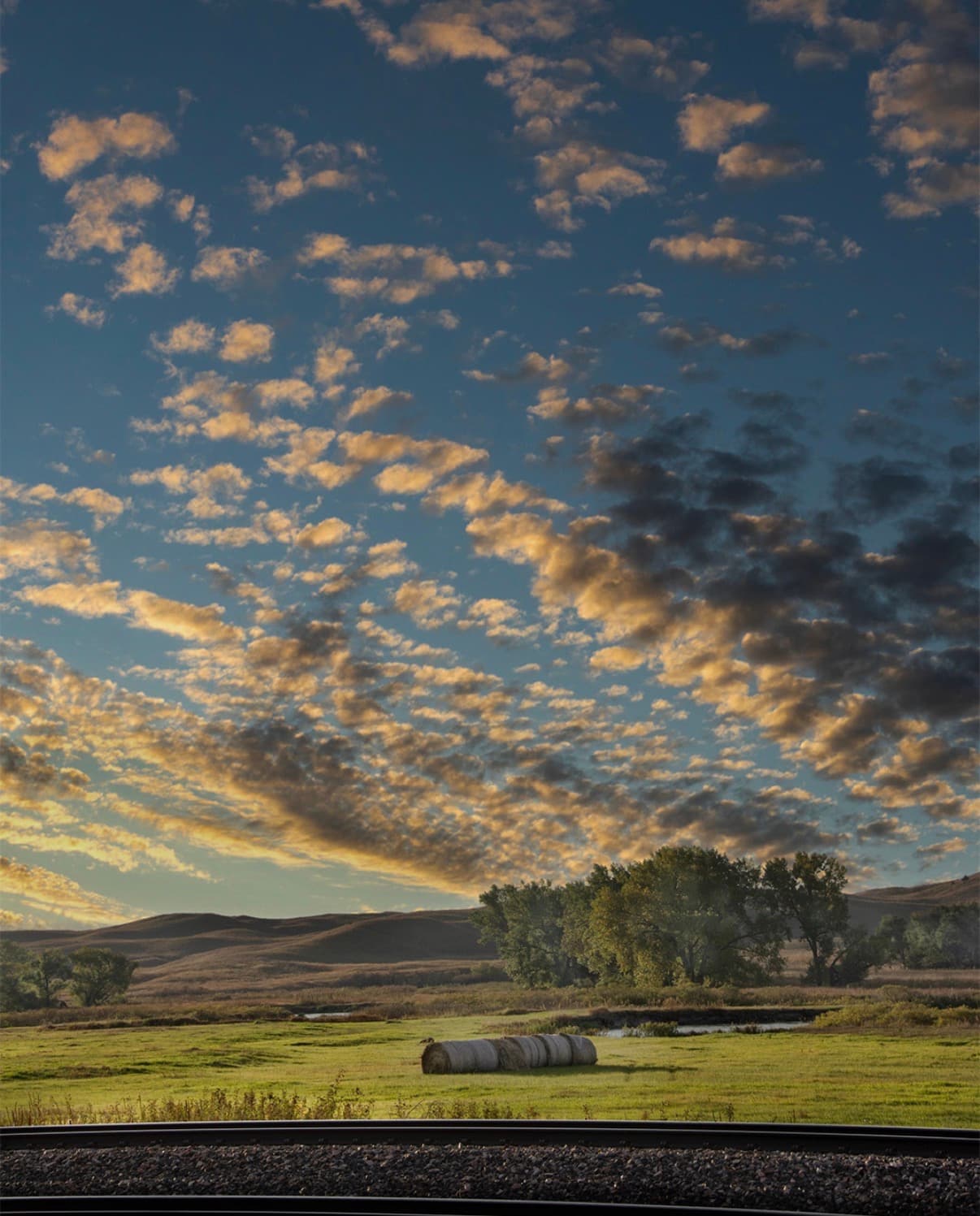 Hay bales in open Nebraska prairie under a sky of gold clouds