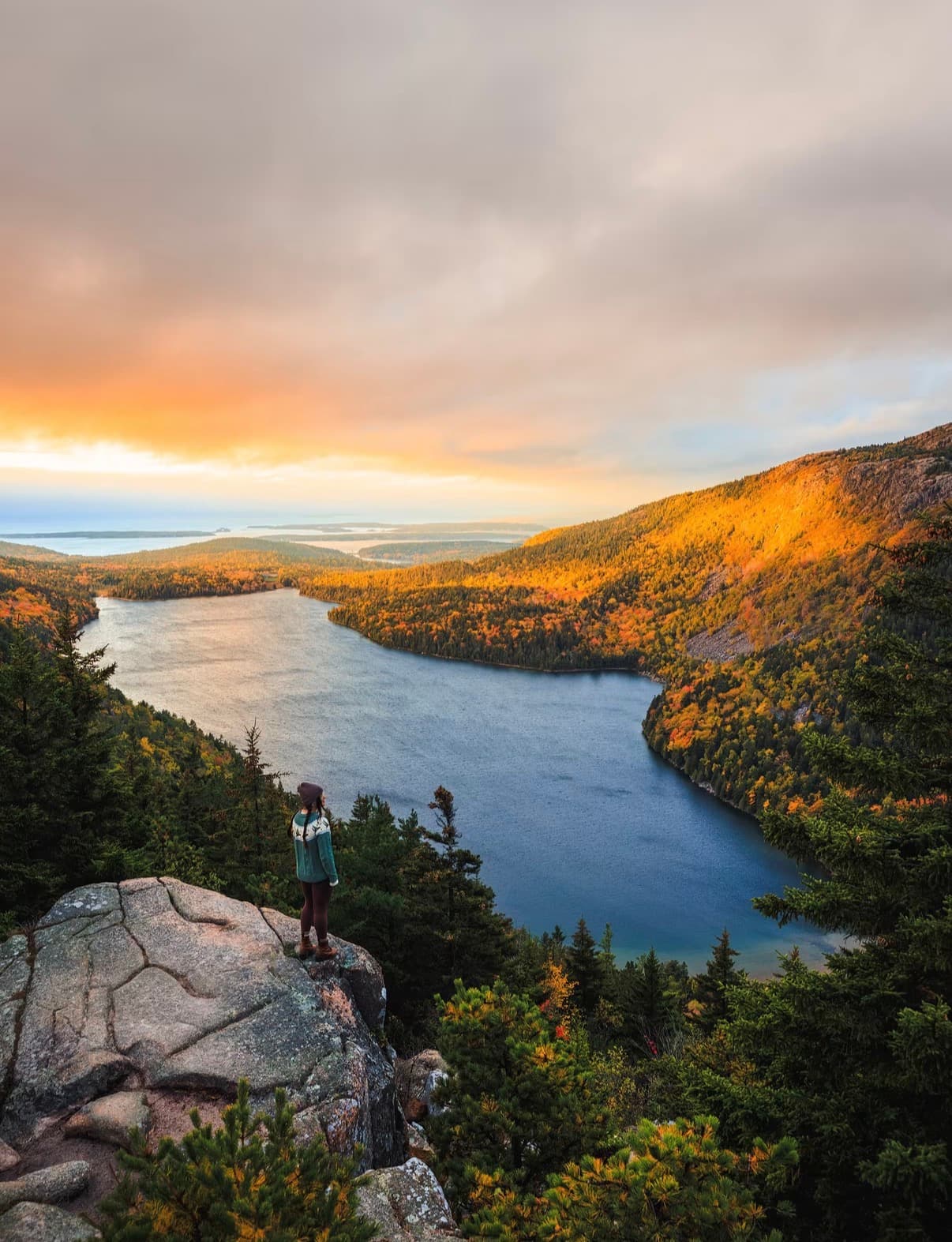 A hiker on a granite ledge above a mountain lake at golden hour