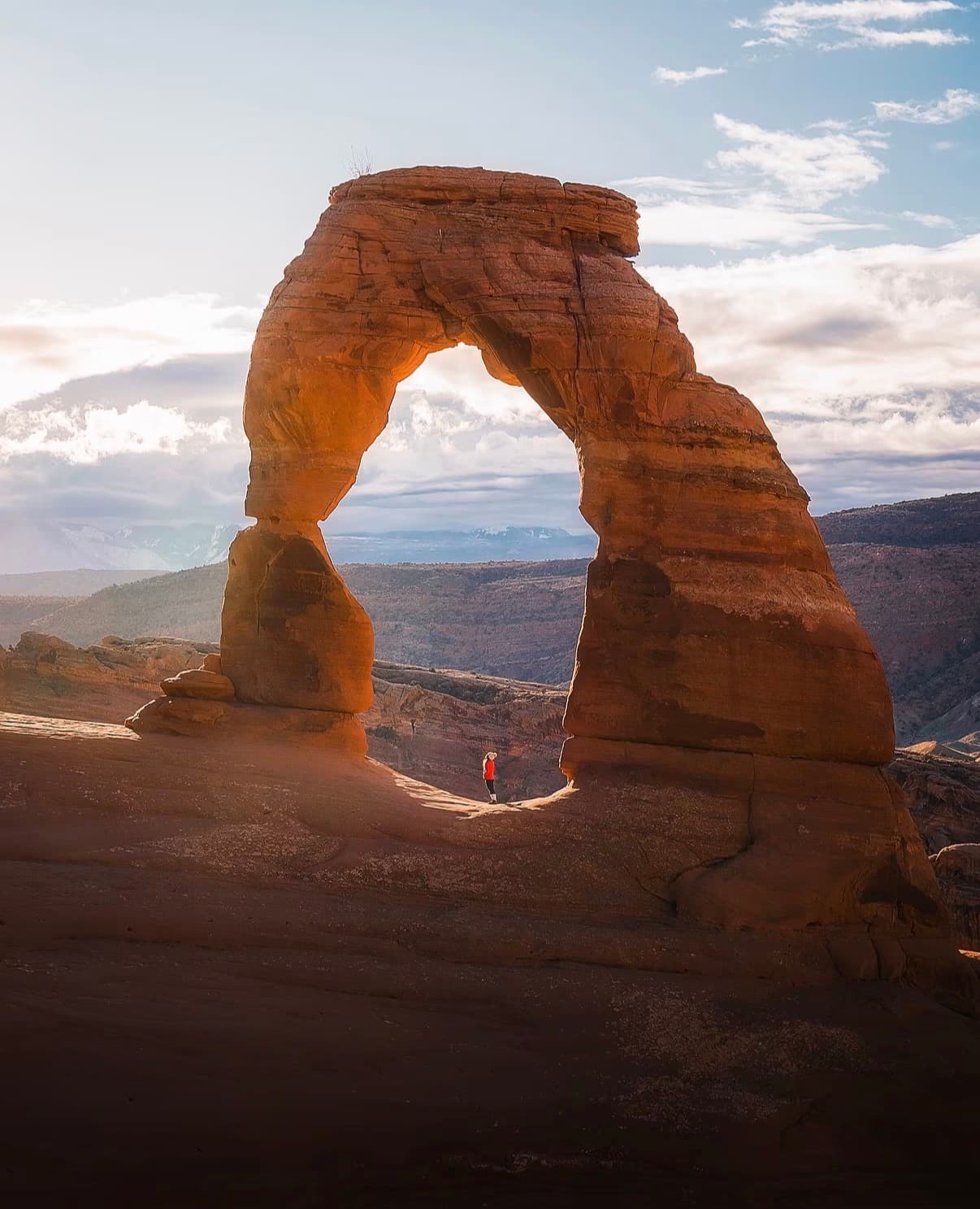 Delicate Arch glowing in late sun above slickrock and distant mountains