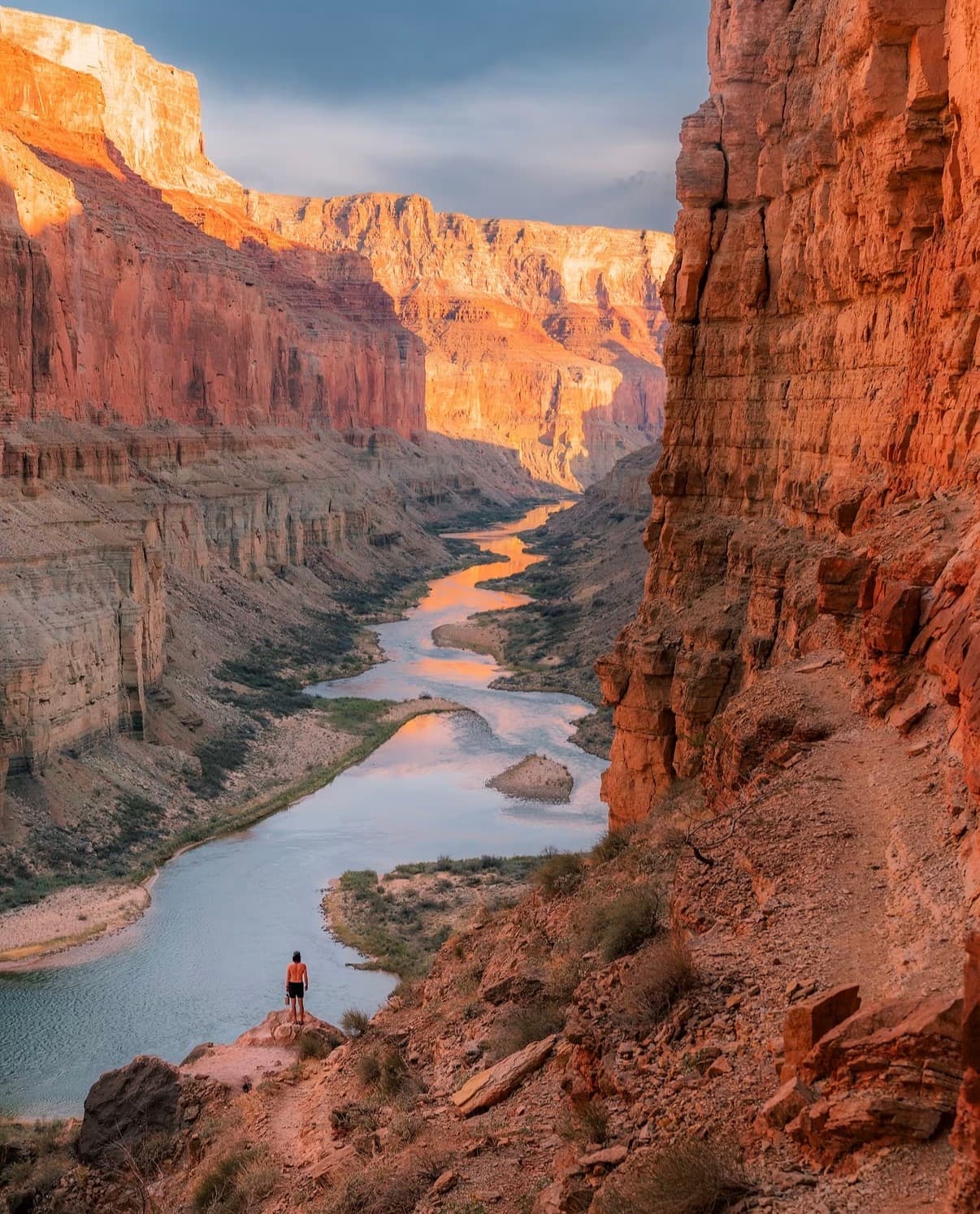 A hiker above the Colorado River deep inside red canyon walls