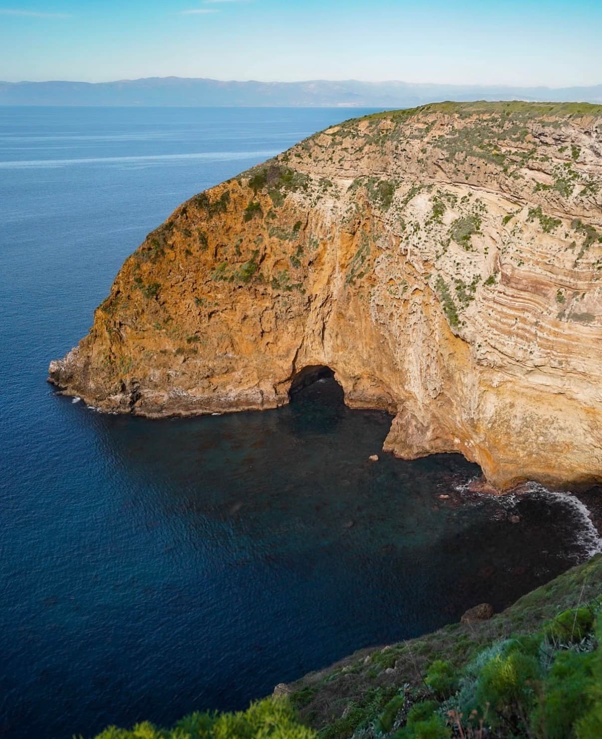 A striped sandstone headland with a sea cave above deep blue water