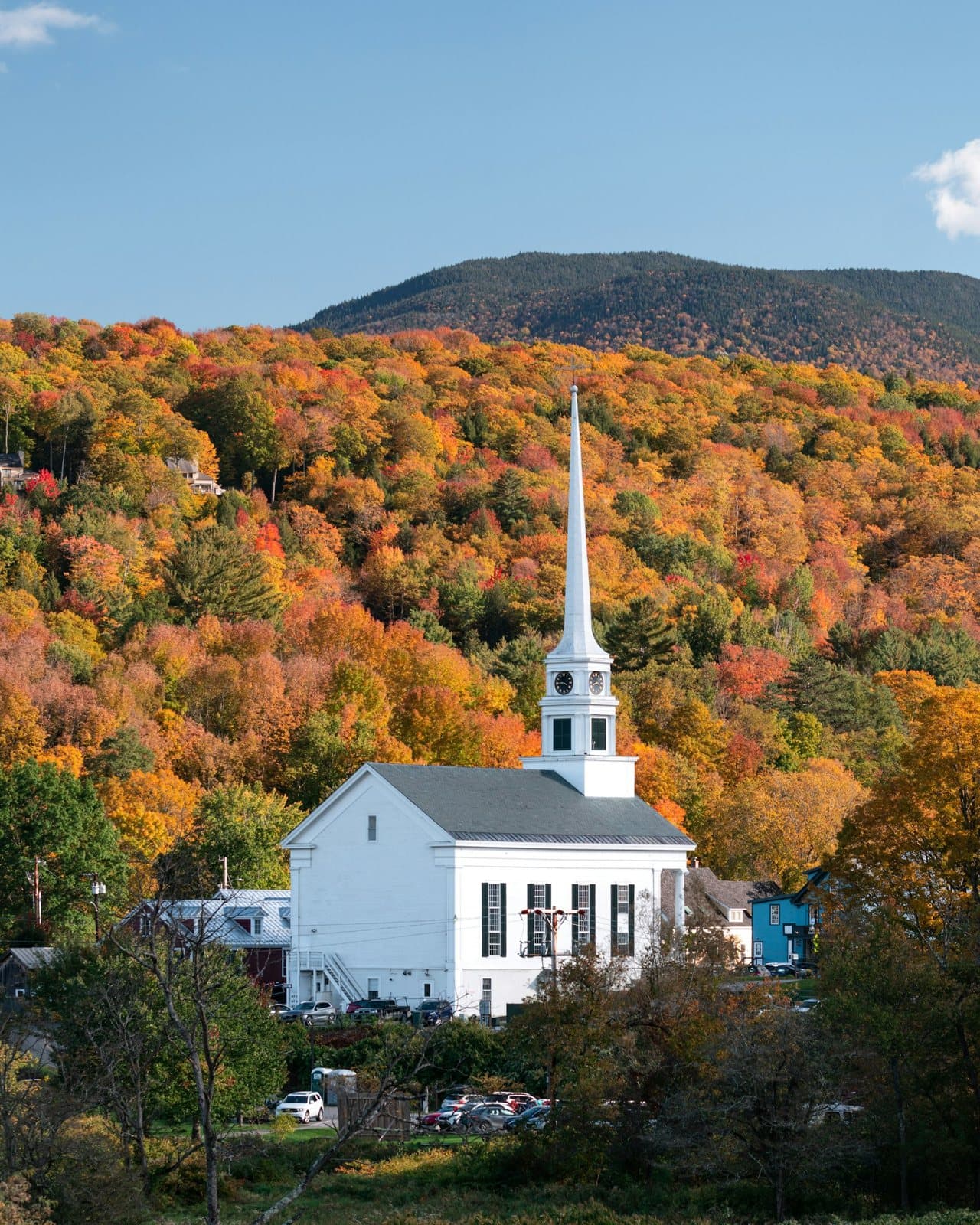 A white church steeple below a hillside of autumn colour in Stowe, Vermont
