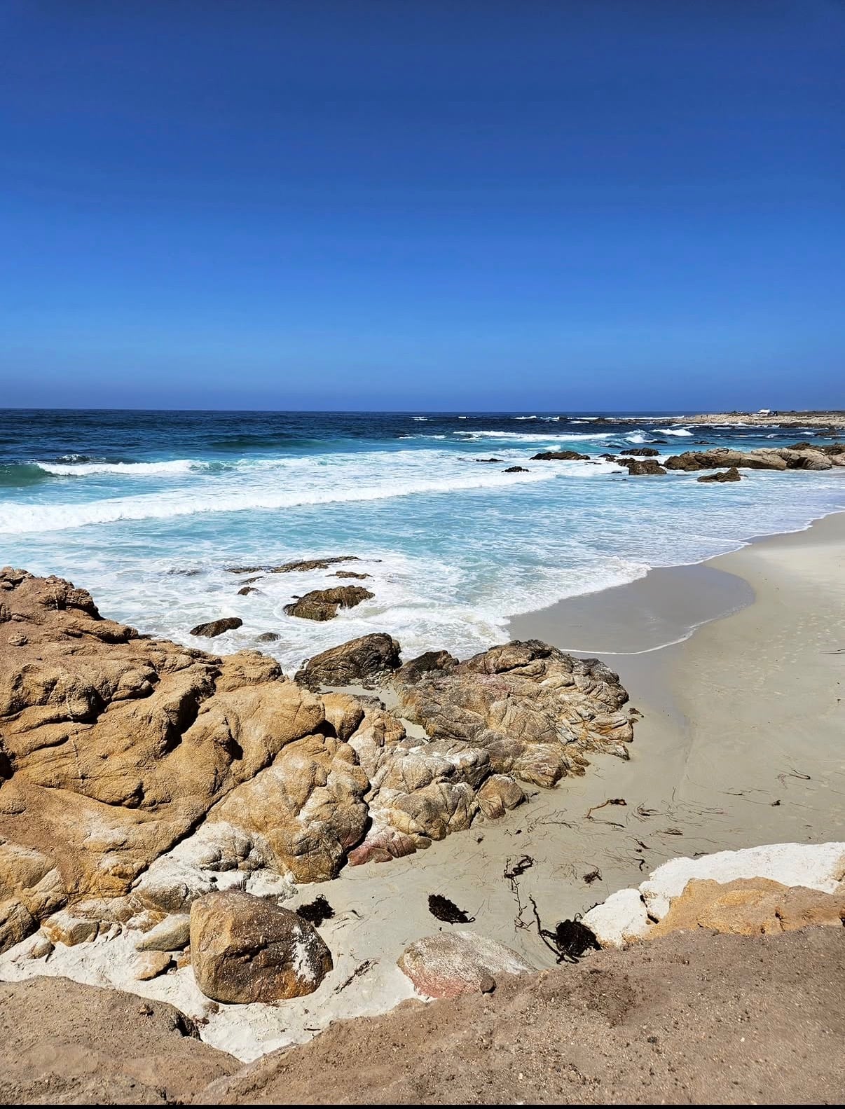 Waves washing onto a pale beach beside weathered rocks