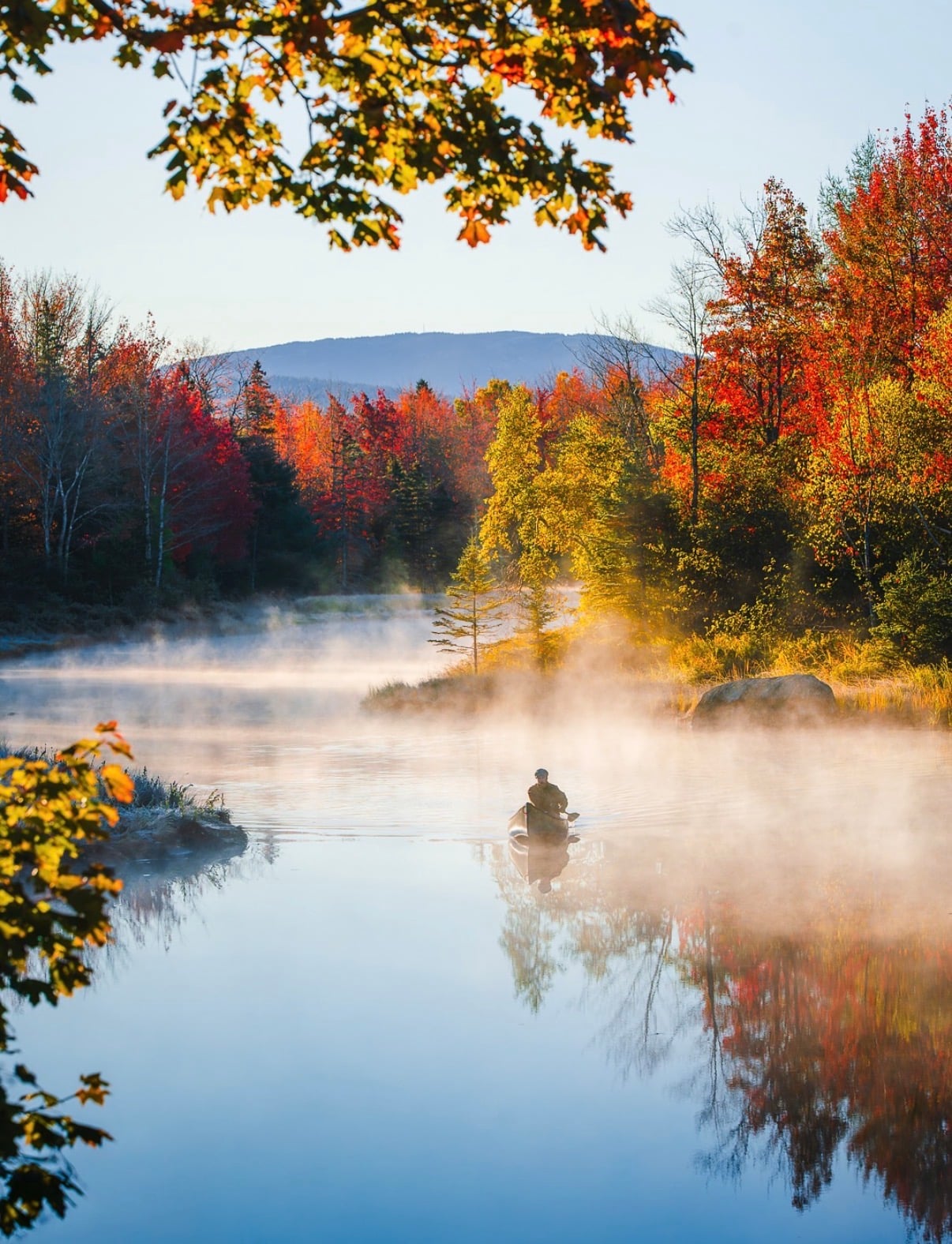 Mist rising off a still lake ringed by autumn trees
