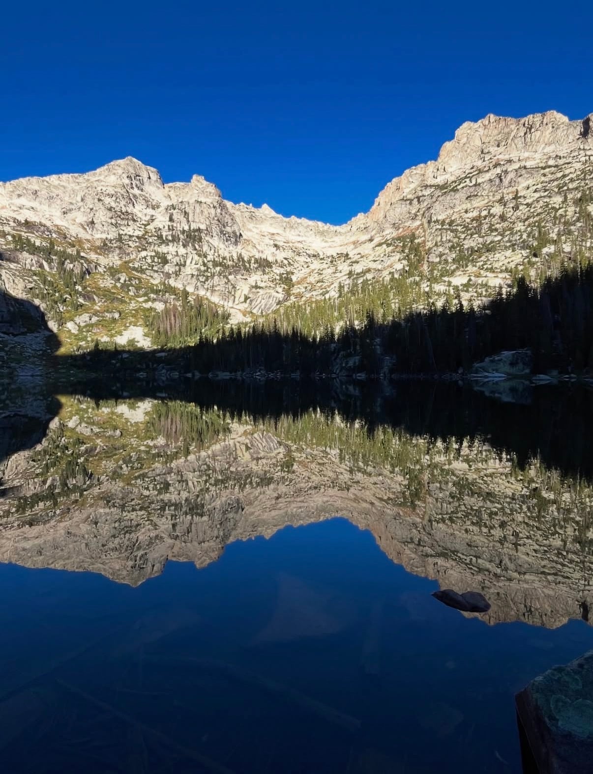 Granite peaks mirrored in a still alpine lake under a deep blue sky