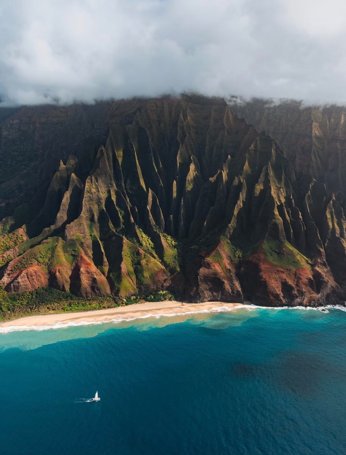 The Nāpali Coast from the air, a catamaran below the fluted green cliffs