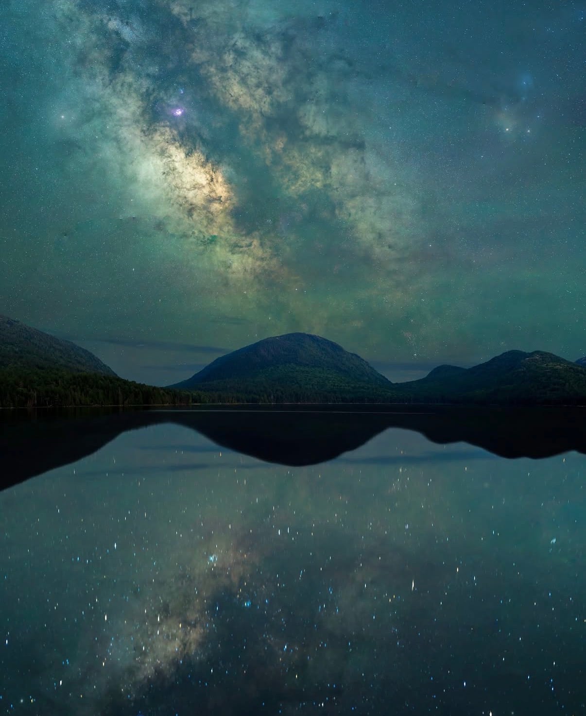 The Milky Way over rounded mountains mirrored in a lake