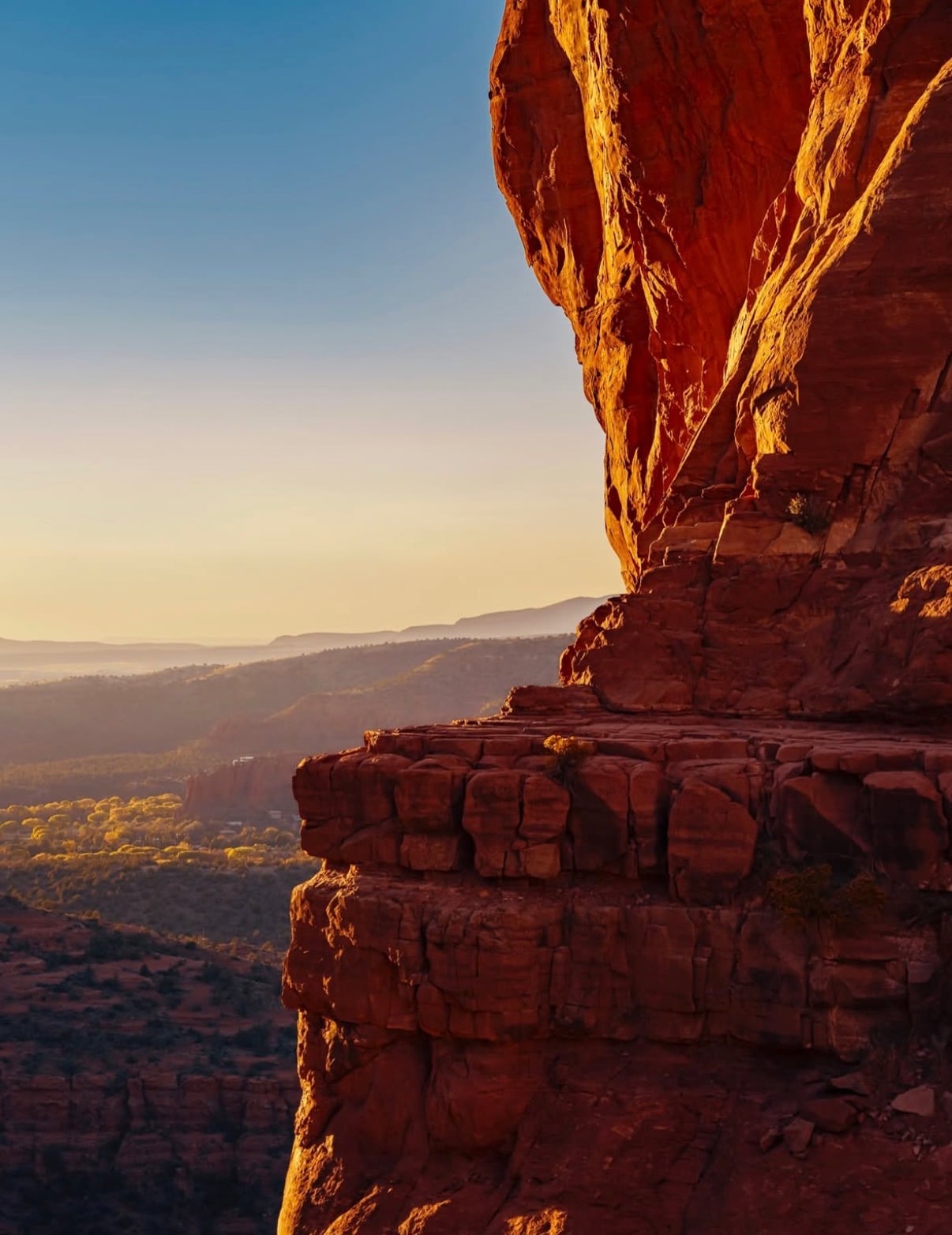 A red-rock pillar lit by low sun above hazy canyon country