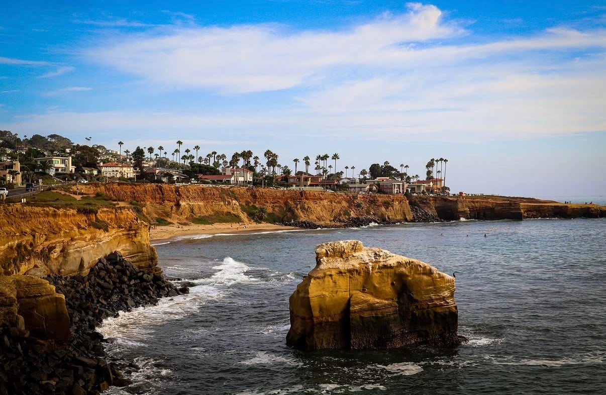 A sandstone sea stack below palm-lined coastal cliffs
