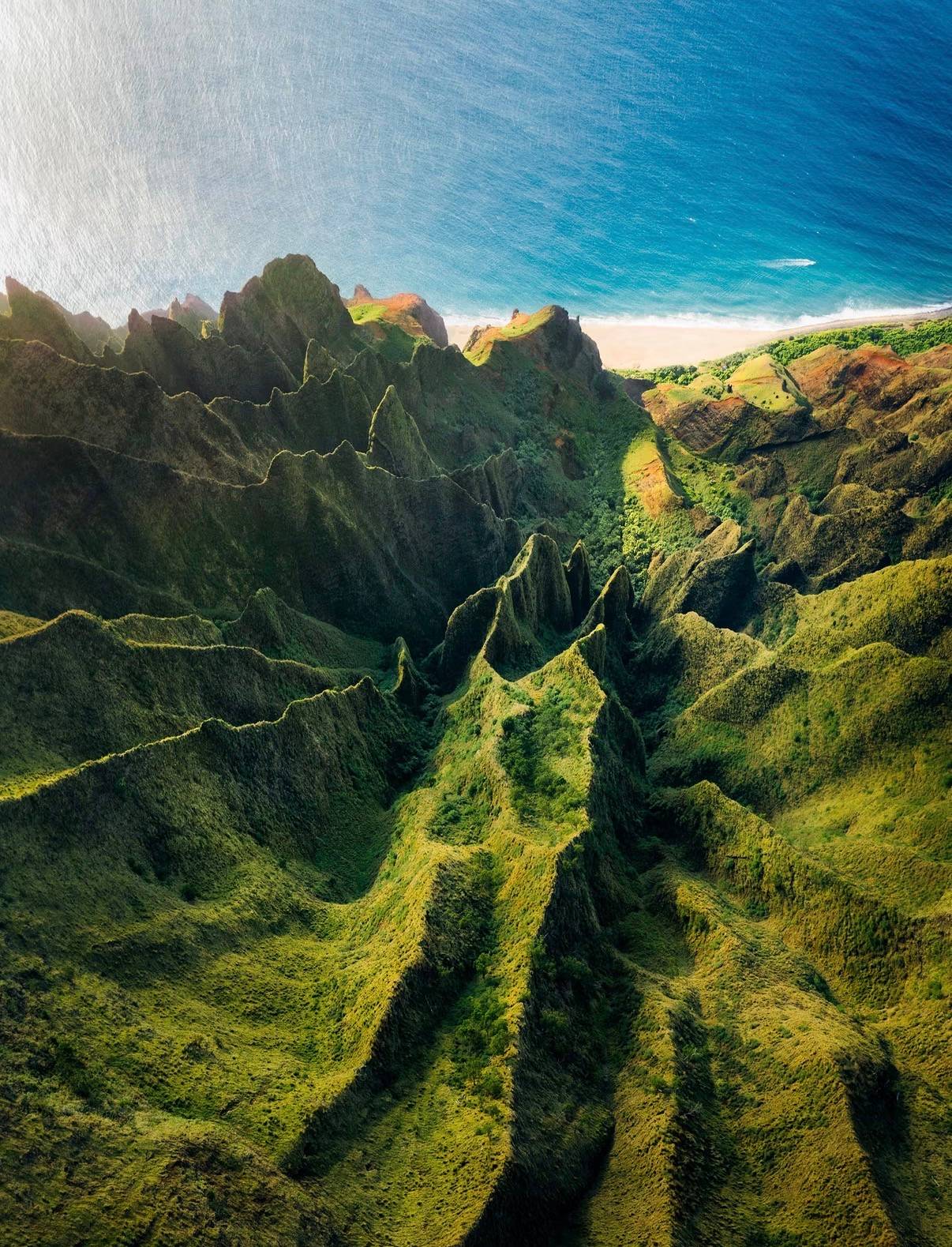 Green fluted ridges running down to a beach on Kauaʻi's north shore