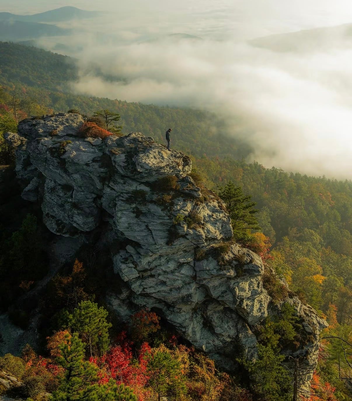 A hiker on a rocky outcrop above a valley filled with cloud