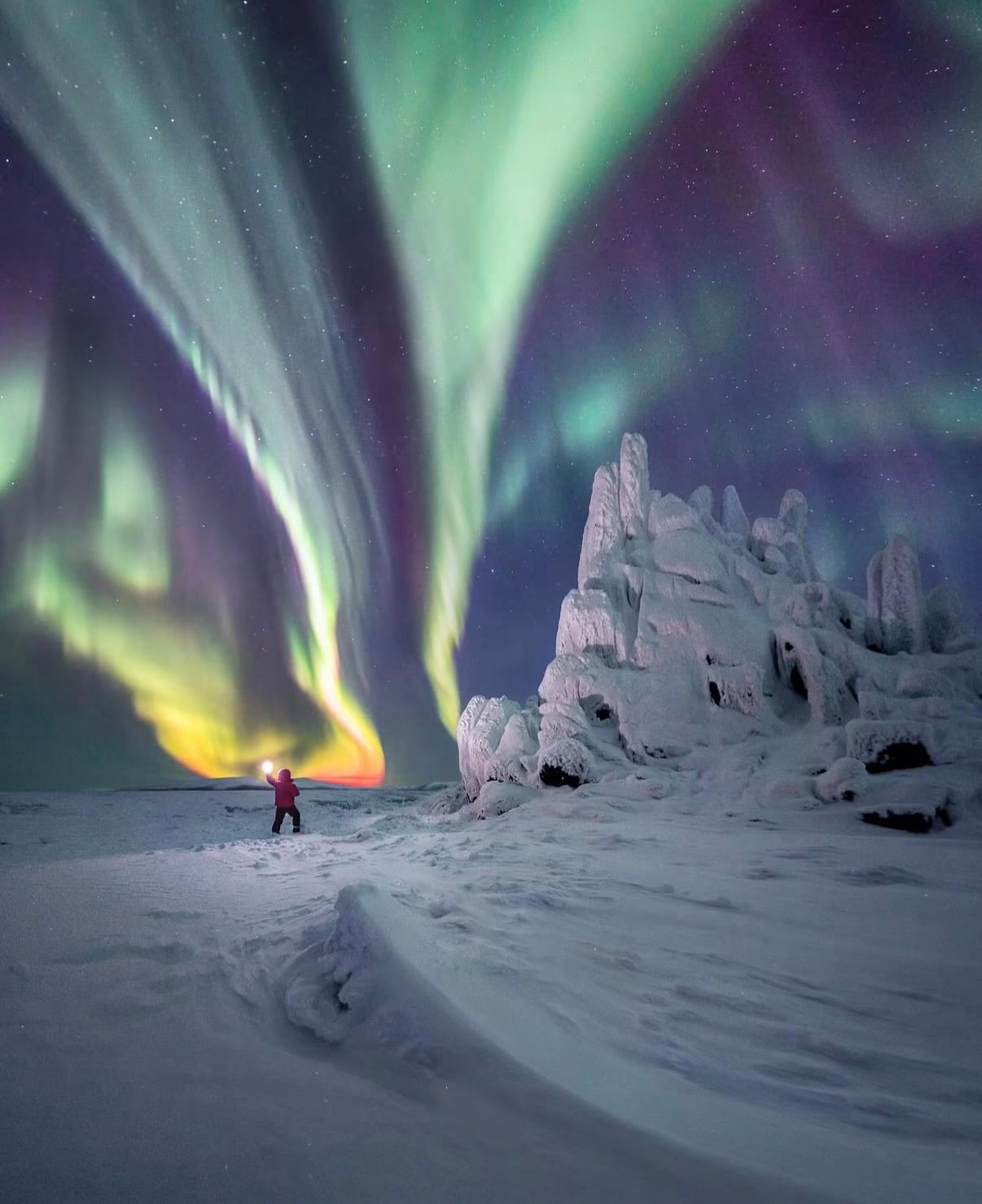Green and violet northern lights over a snowfield, with a traveller holding a lamp