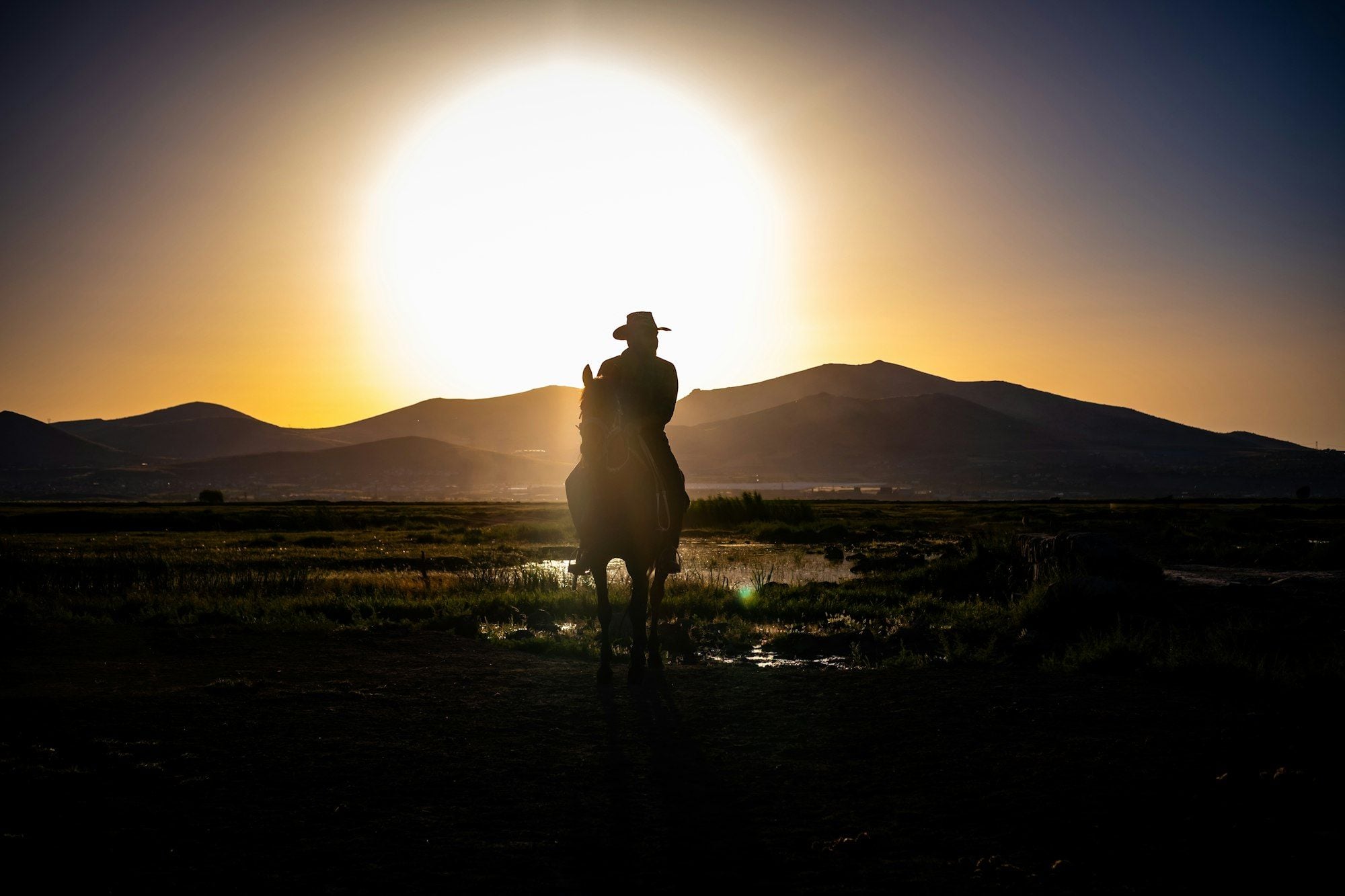 A rider on horseback, small against the hills, with the sun setting behind