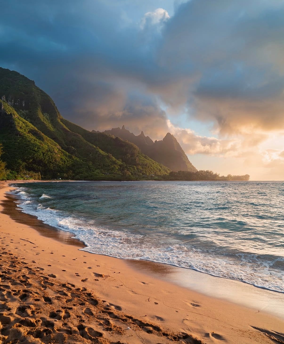 Tunnels Beach on Kauaʻi at sunset, with the Nāpali peaks under storm clouds