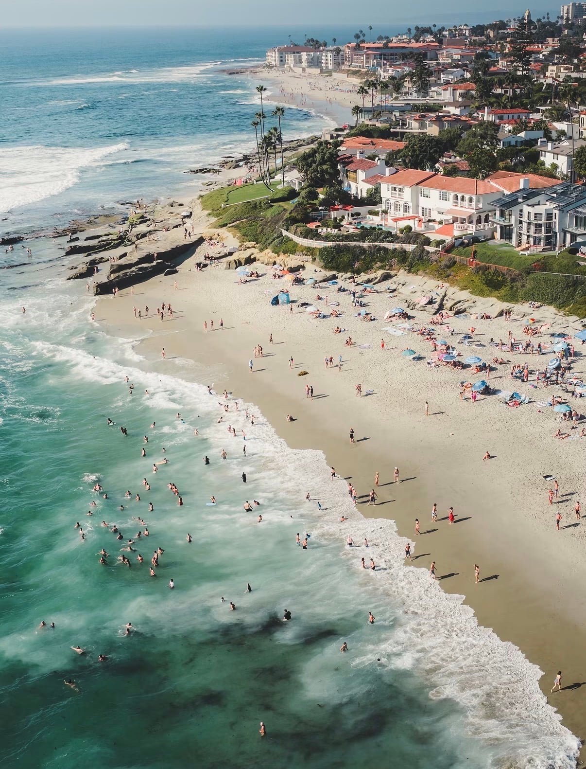 An aerial view of a crowded La Jolla beach with surf rolling in beside clifftop houses