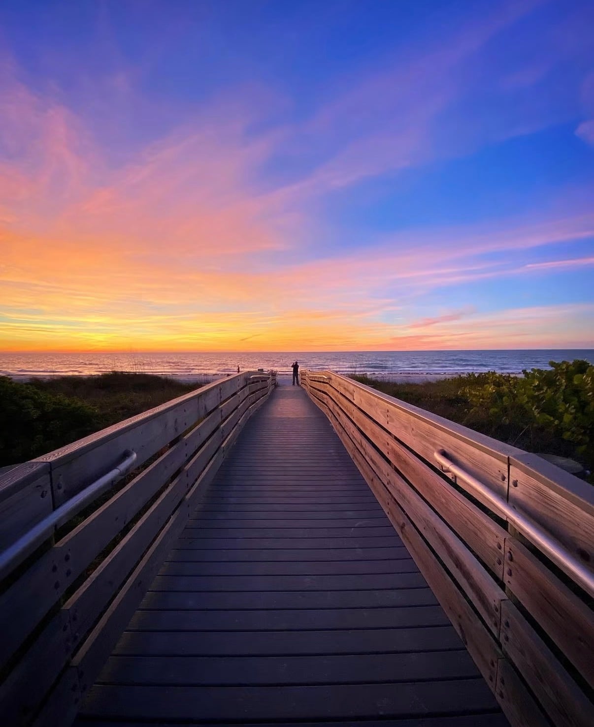 A wooden boardwalk leading over the dunes to the sea at sunset