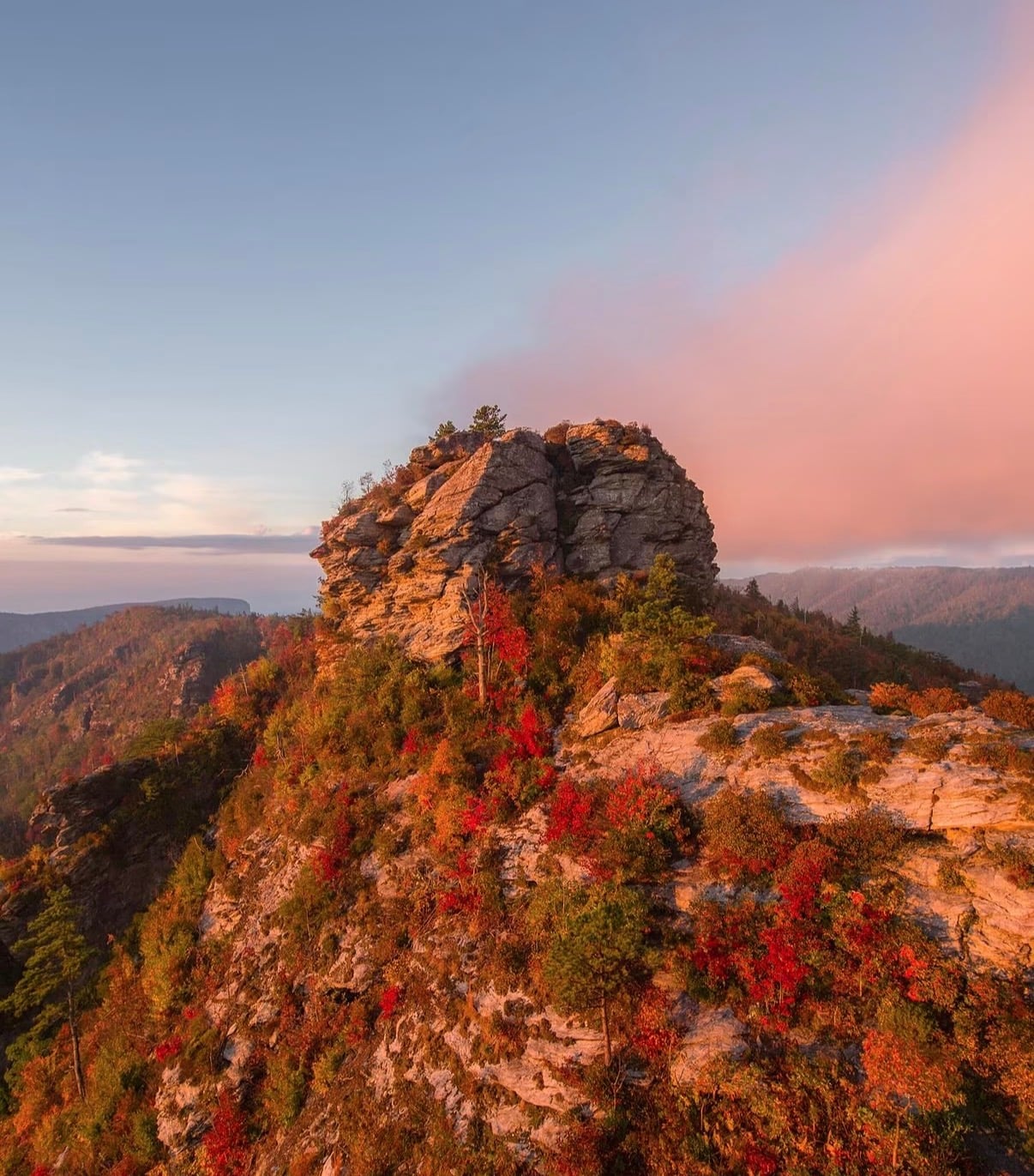 A craggy rock summit above slopes of red autumn leaves at dusk