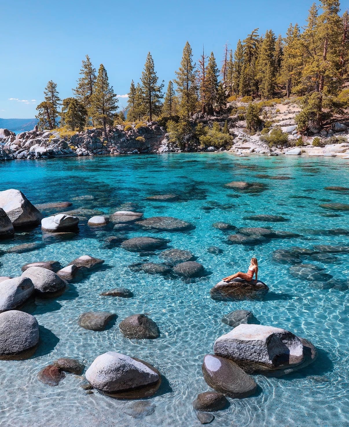 A swimmer on a boulder in clear turquoise water on the Lake Tahoe shore