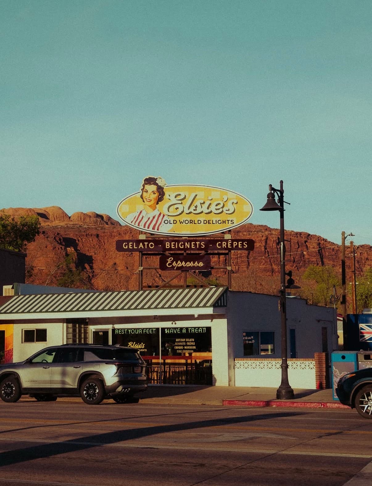 A retro café sign on a Moab street below red-rock cliffs