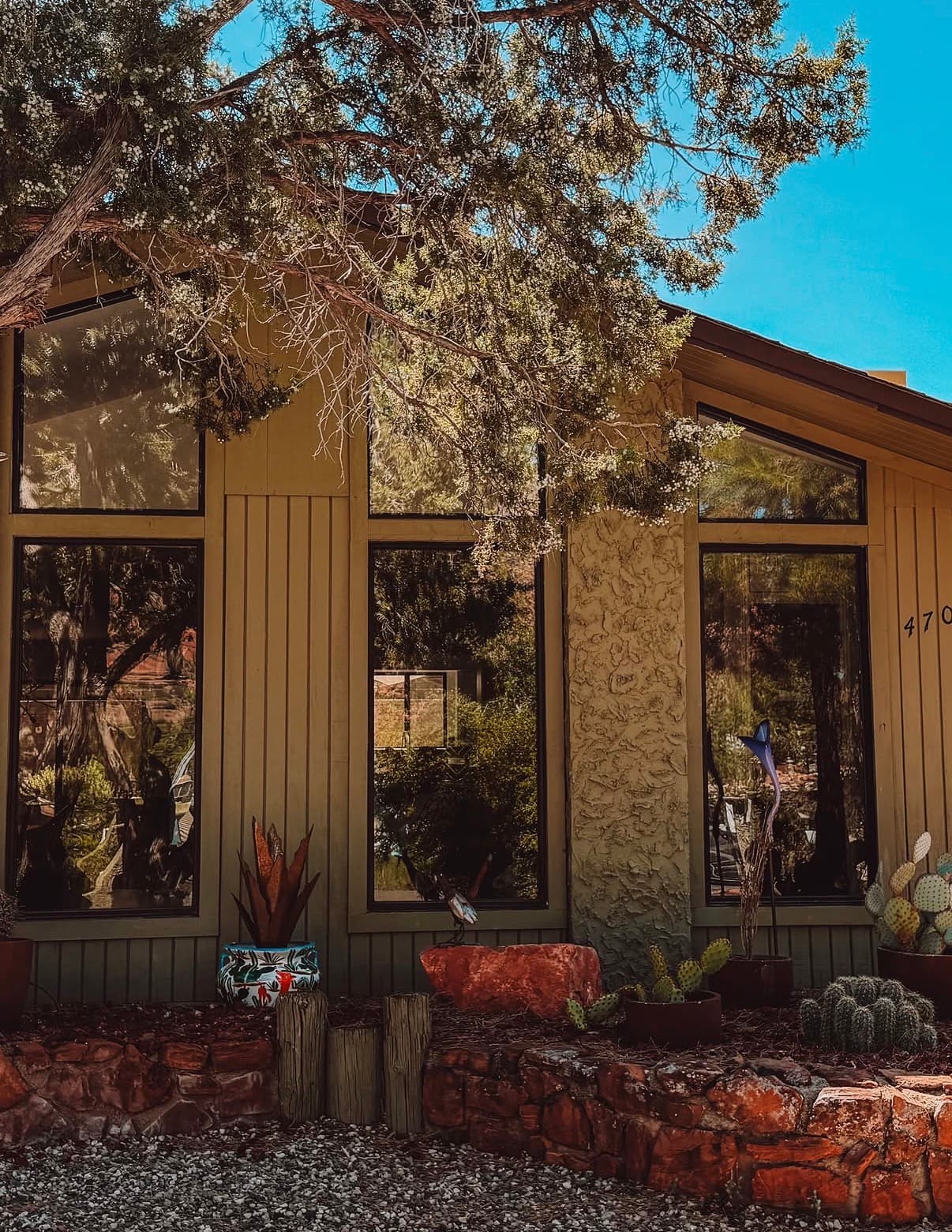 A wooden-clad Sedona house with red-rock garden beds under a juniper